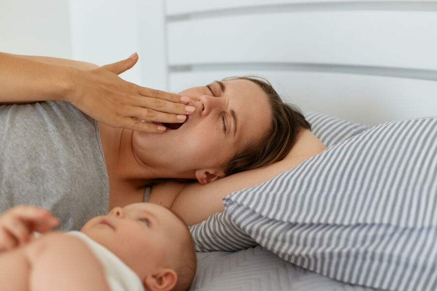 Imagem indoor-portrait-tired-mother-lying-bed-with-little-baby-girl-boy-yawning-covering-mouth-with-palm-looks-sleepy-having-lack-energy-sleepless-nights 1